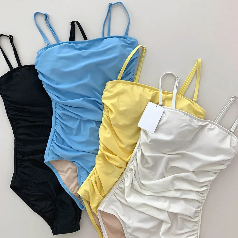Sling neck one-piece swimsuit with belly pleating in slim-fit design, available in blue, white, yellow, and black colours