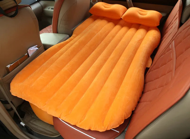 Black inflatable car bed with flocked material and two pillows, set up in a car's rear seats.