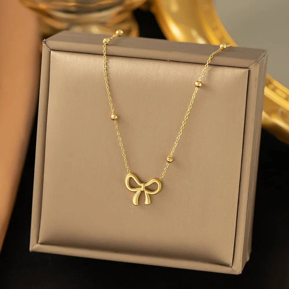 Gold electroplated bow design necklace with cross chain on white background
