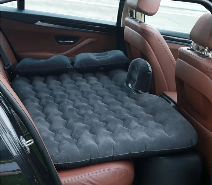 Black inflatable car bed with flocked material and two pillows, set up in a car's rear seats.