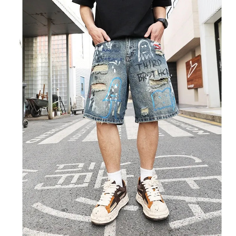 Blue men's ripped denim shorts with graffiti-style detailing and straight-leg cut.