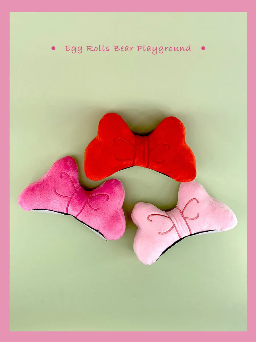 Soft plush bow tie decoration for a motorcycle or ski helmet in red, peach pink, and rose pink colours.