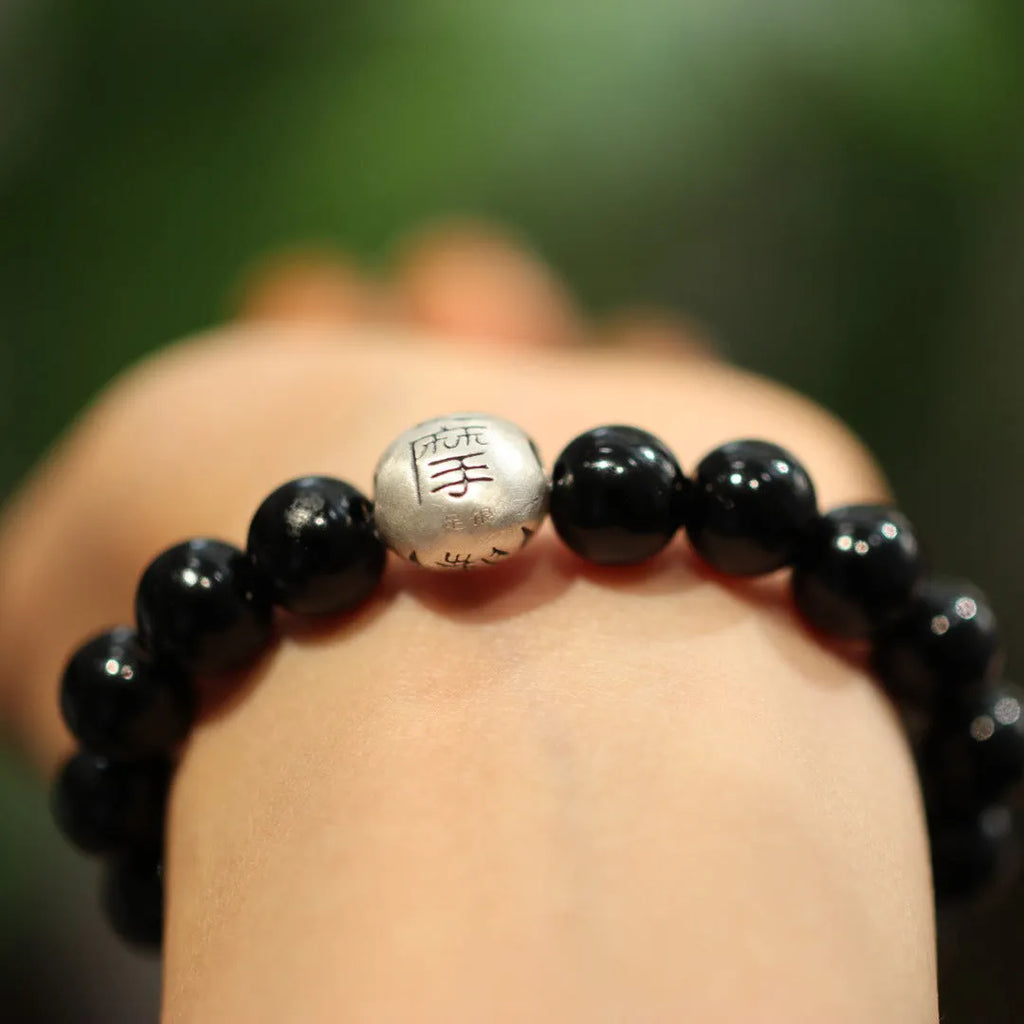 Close-up of a bracelet with large round black agate beads and a sterling silver clasp on a wrist.
