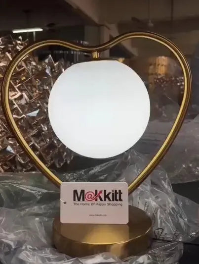 Pink heart shaped acrylic table lamp on a table next to a bed.