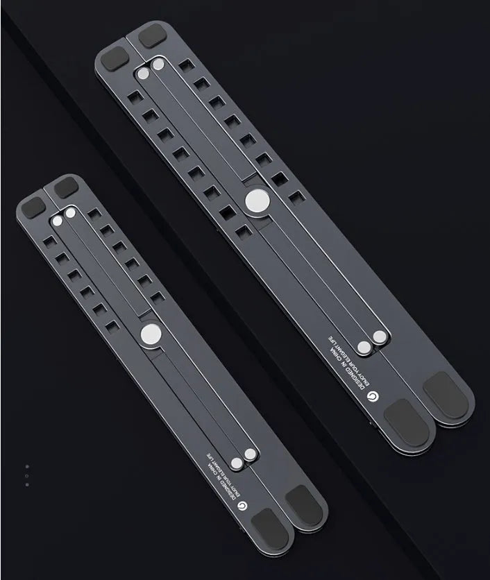 Deep grey portable aluminium laptop stand, folded flat next to an open laptop showing its adjustable height.
