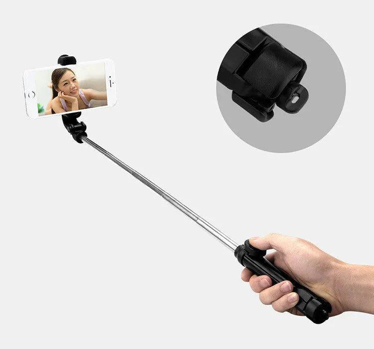 Black Bluetooth selfie tripod with extended stand and 360-degree rotating phone clip attached to an iPhone.
