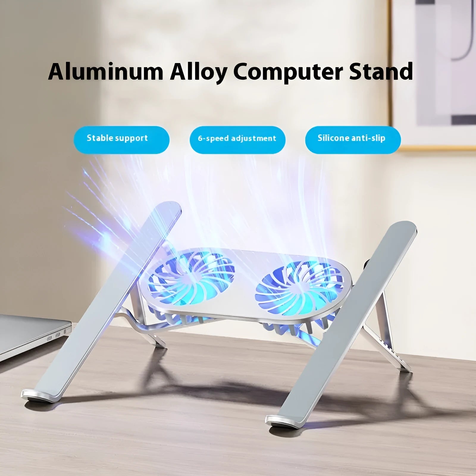 Silver aluminium laptop stand with twin fans raised at an angle on a wooden desk.