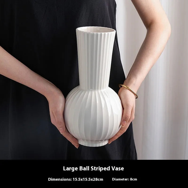 White ceramic ball vase with blue stripes and artificial blue orchid flowers on a wooden table.