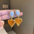 A pair of oval-shaped, pleated love heart stud earrings in alloy, shown in various colours.