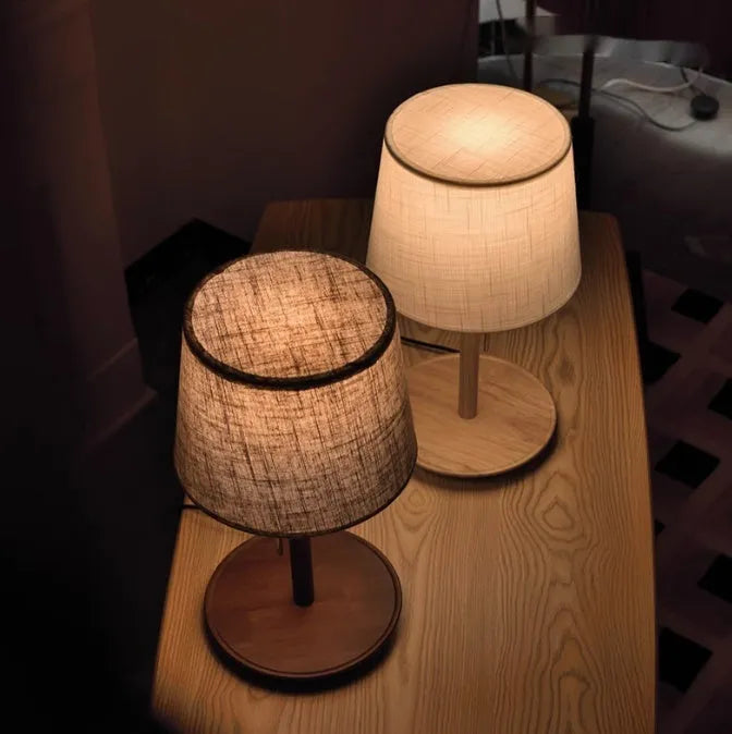 Walnut colour solid wood bedside lamp with white cloth shade on a wooden table.