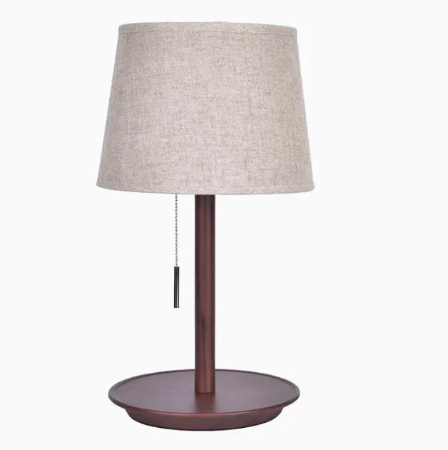 Walnut colour solid wood bedside lamp with white cloth shade on a wooden table.