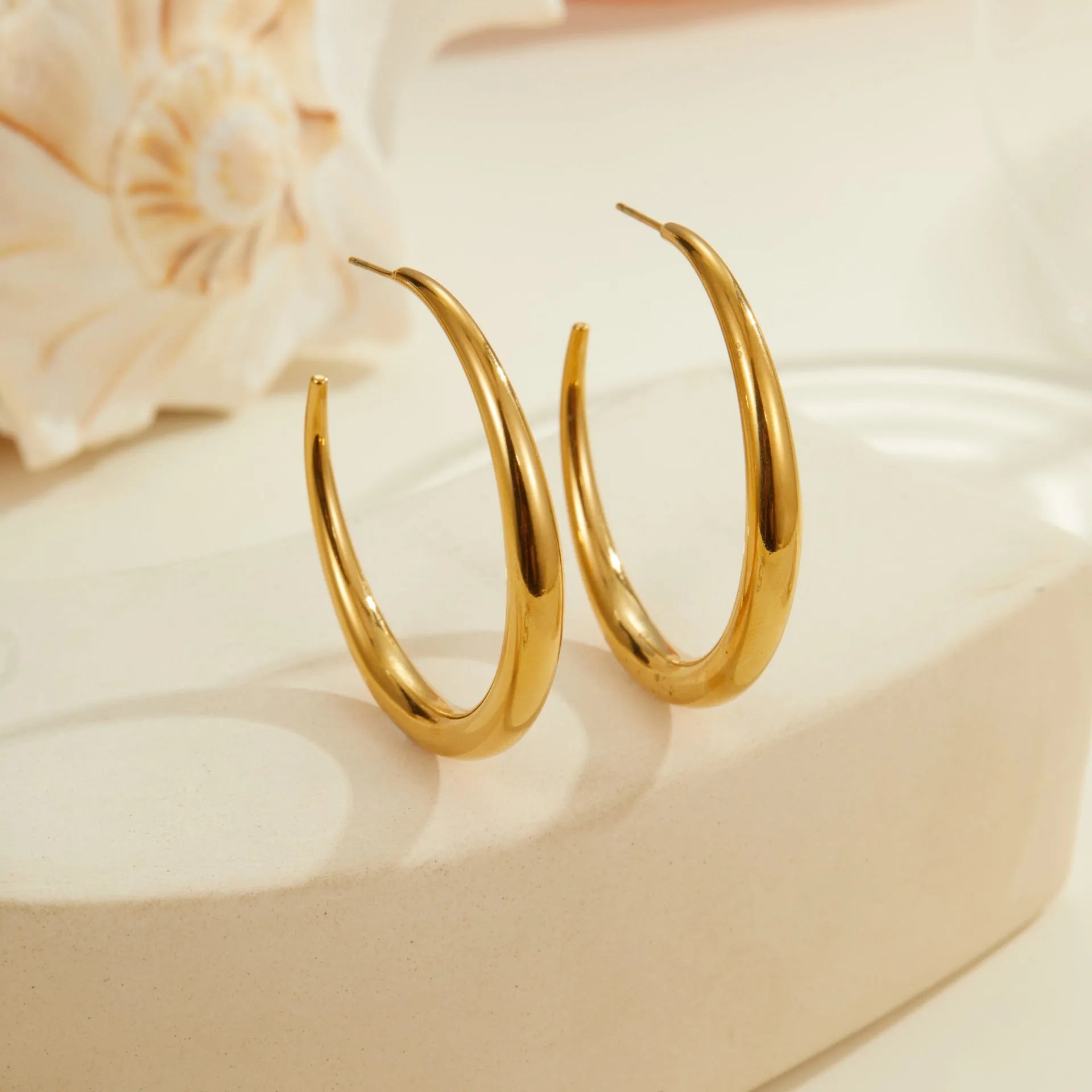 A pair of simple round titanium steel hoop earrings in a gold finish on a white background.