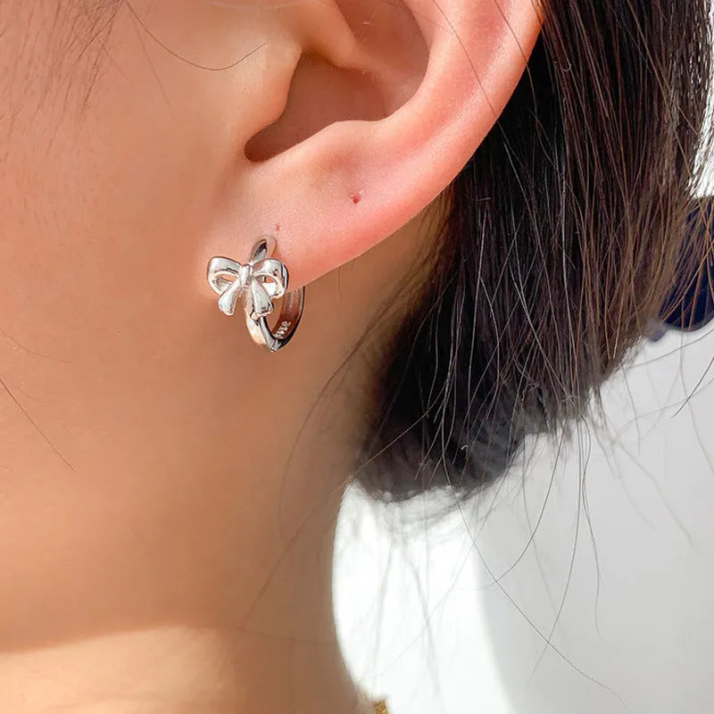 Pair of 925 sterling silver bow earrings with electroplated silver finish on white background