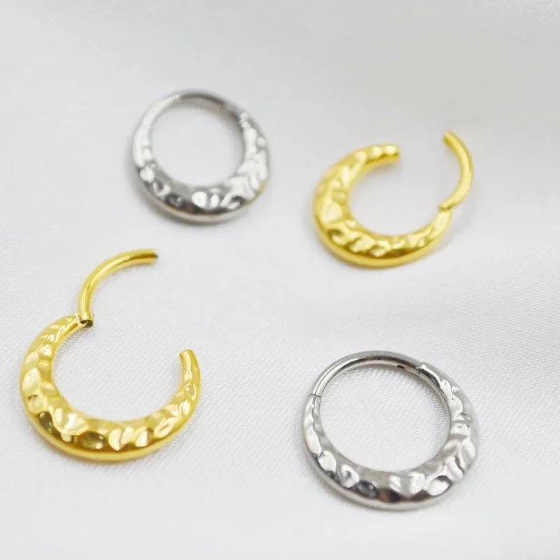 Close-up of a concave-convex titanium nose ring in gold finish on a grey background.