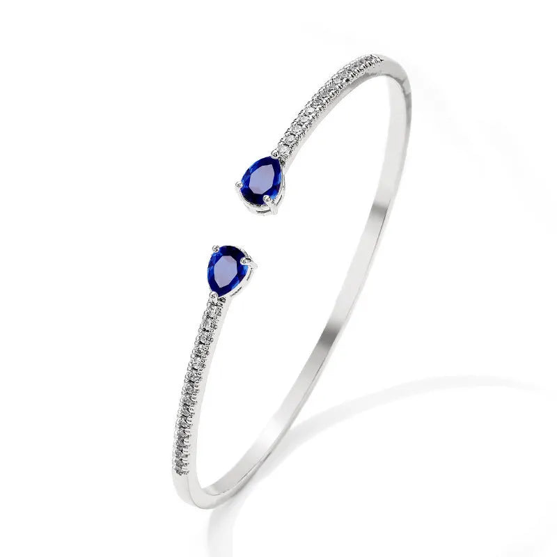 Close-up of a solid copper bracelet with inlaid white zircon stones on a blue background.