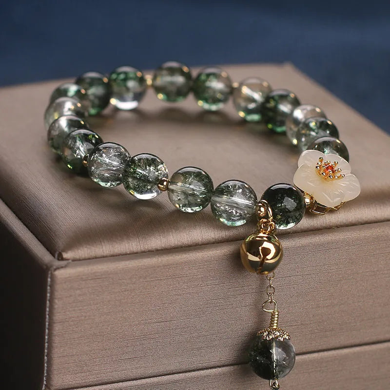 Green Phantom quartz crystal bracelet with white jade flower on a plain background