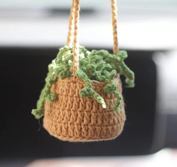 Green and white knitted wool car plant decoration with hanging rope on a car dashboard