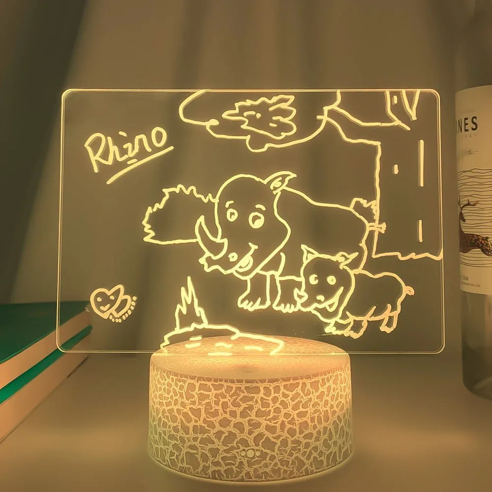 Black 3D acrylic night light with handwritten message board, remote control, and marker pen on desk.