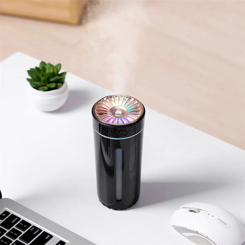 Black portable ultrasonic humidifier with colourful LED lights, shown next to a USB cable on a desktop.
