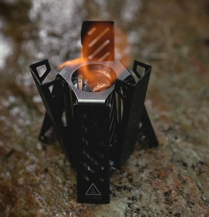Black hexagon foldable alcohol stove for outdoor camping on a wooden surface.