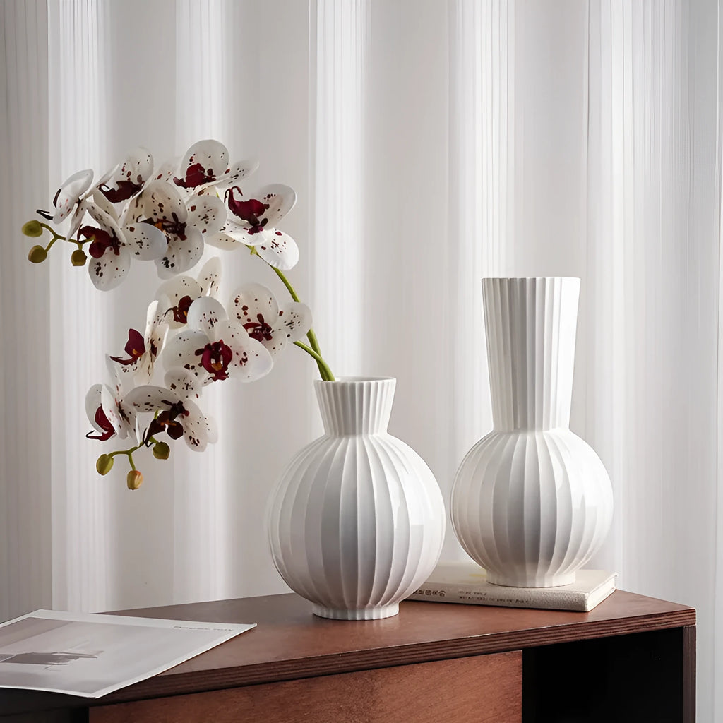 White ceramic ball vase with blue stripes and artificial blue orchid flowers on a wooden table.