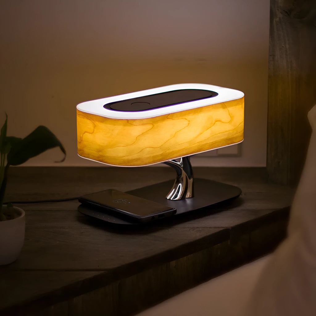 Creative tree light table lamp with natural cherry veneer shade, Bluetooth speaker, and wireless charging on a bedside table