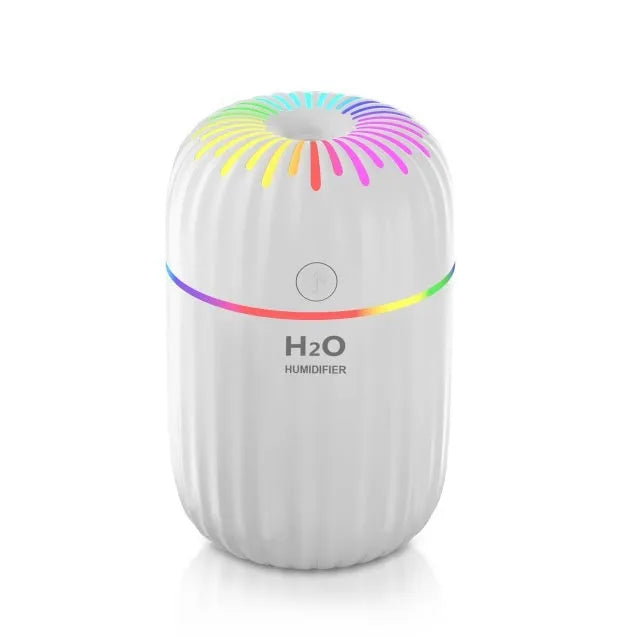 White USB personal mini humidifier with fireworks design on a wooden desk next to a laptop.