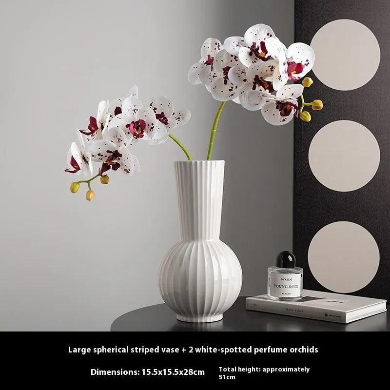 White ceramic ball vase with blue stripes and artificial blue orchid flowers on a wooden table.