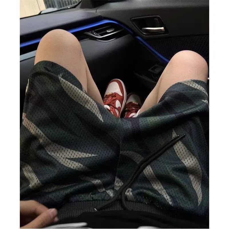 Men's straight cut camouflage mesh shorts in multi-tone green on a hanger.