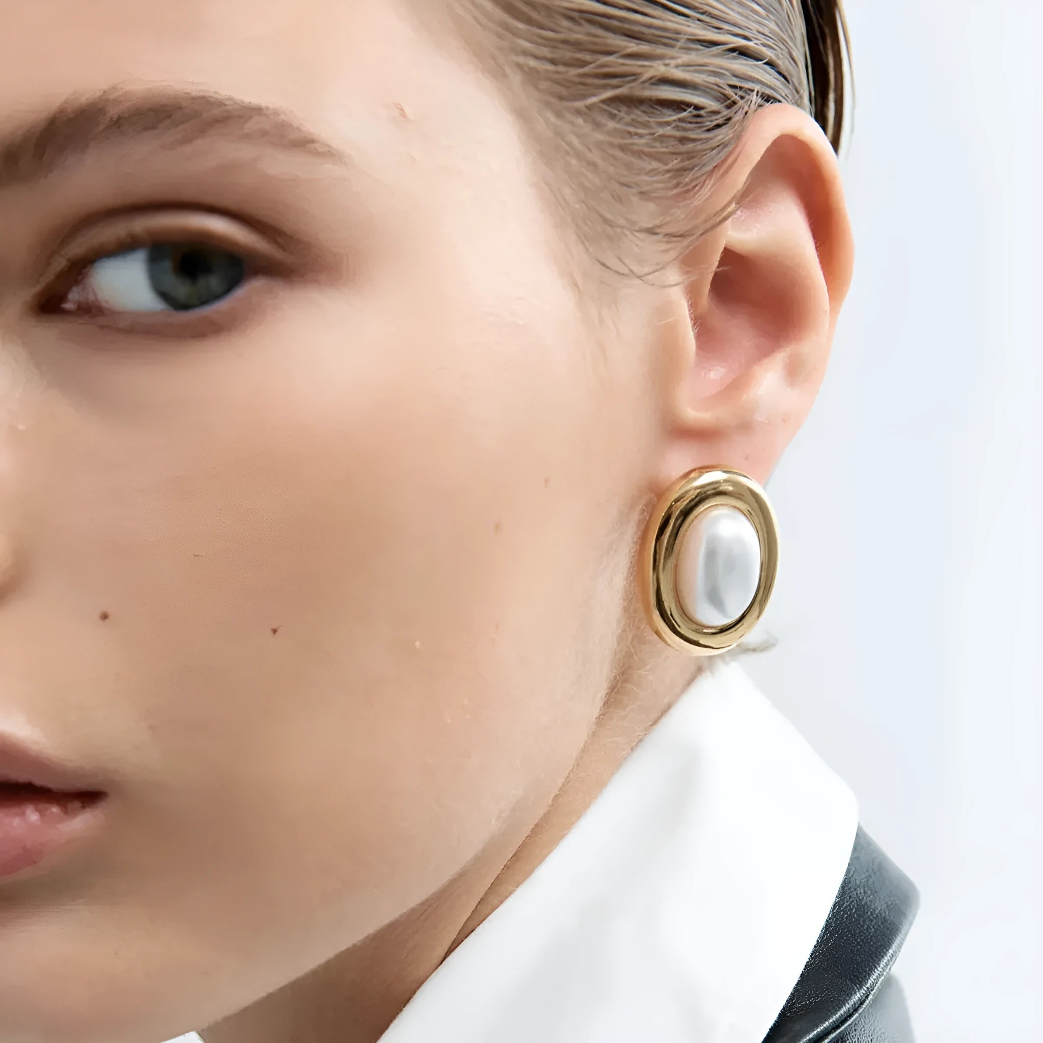 A pair of silver-colour stainless steel stud earrings with a small white pearl detail on a grey background.