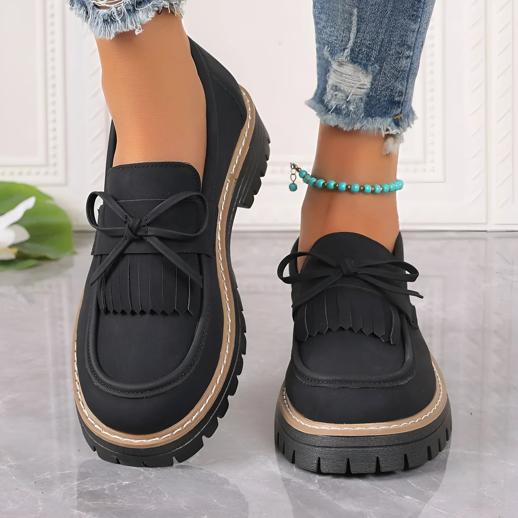 Black plus-size women's loafers with a bow and tassel detail on a chunky rubber sole.