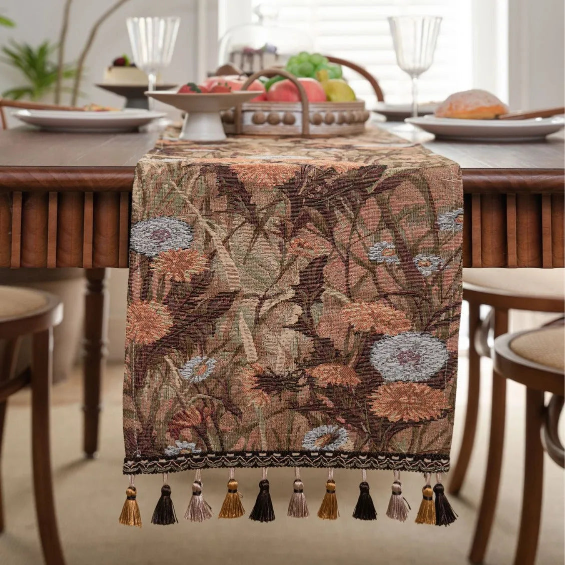 Beige jacquard table runner with floral pattern and long tassels on a wooden table.