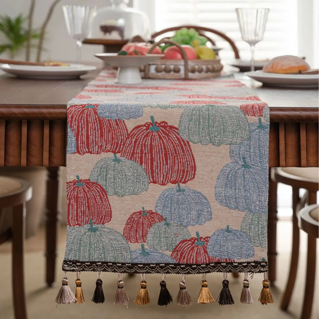 Beige jacquard table runner with floral pattern and long tassels on a wooden table.