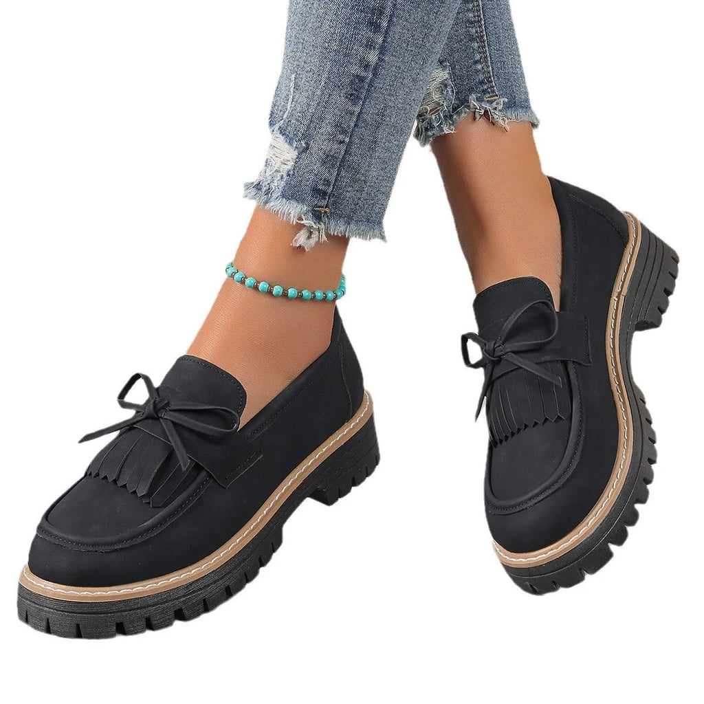Black plus-size women's loafers with a bow and tassel detail on a chunky rubber sole.