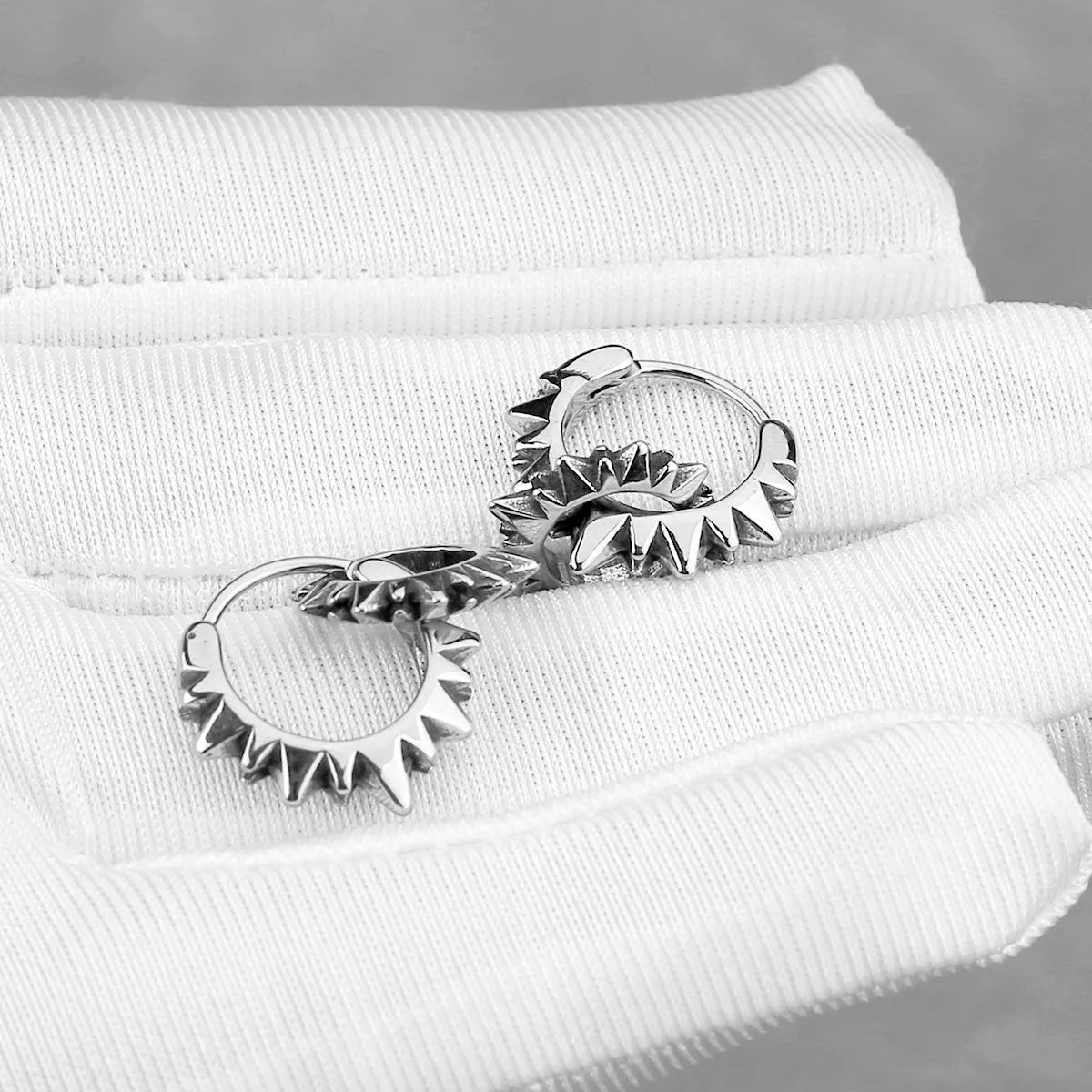 A pair of polished stainless steel round ring earrings in a steel colour on a plain background.
