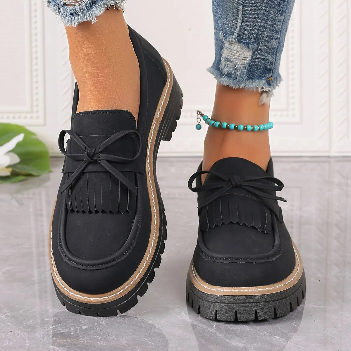 Black plus-size women's loafers with a bow and tassel detail on a chunky rubber sole.