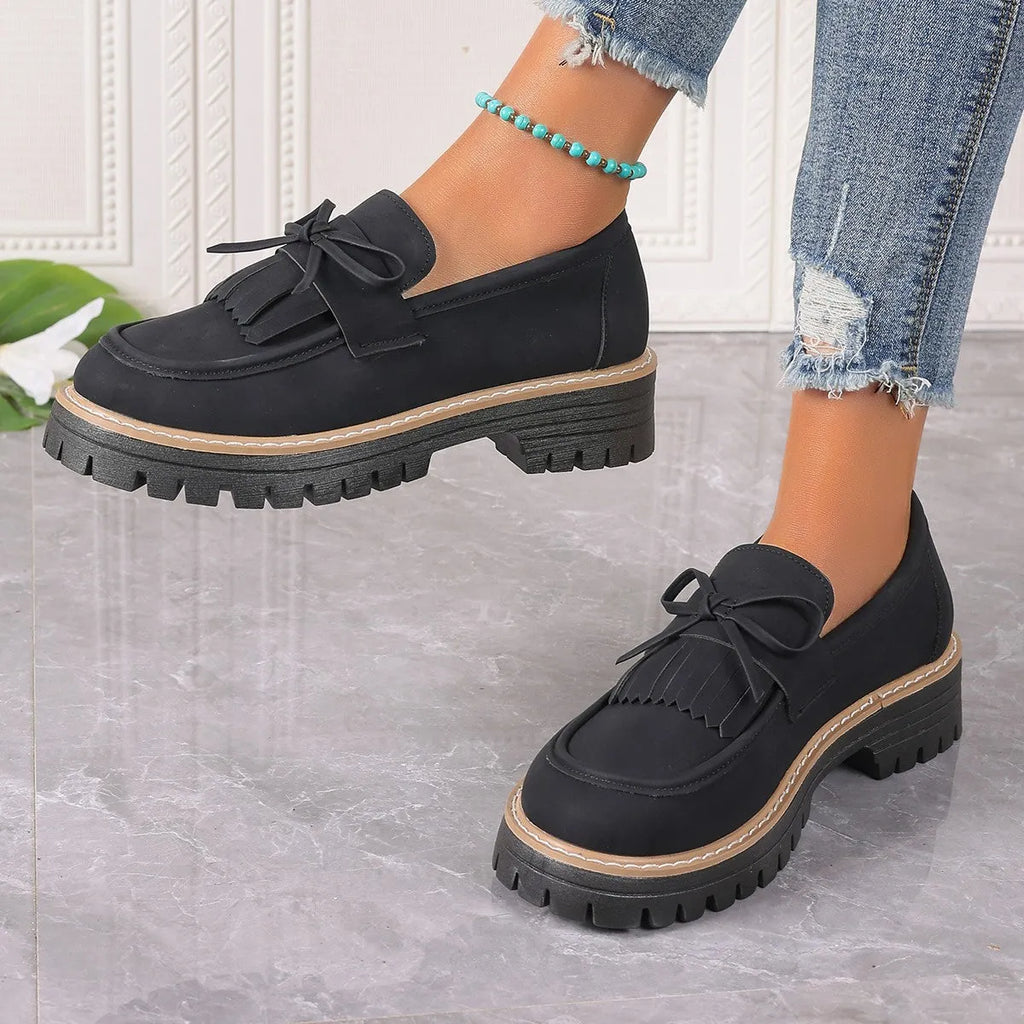 Black plus-size women's loafers with a bow and tassel detail on a chunky rubber sole.