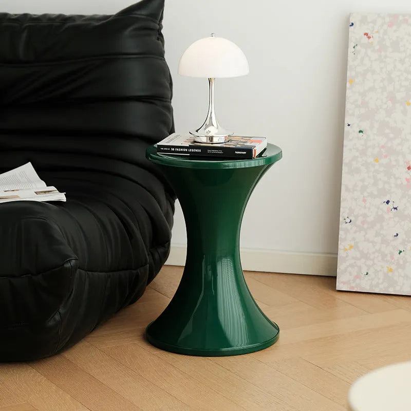 A plastic hourglass-shaped shoe changing stool in green colour on a wooden floor.