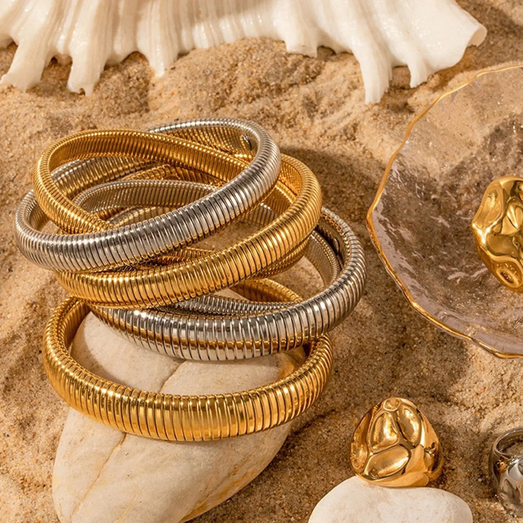 Close-up of a women's titanium steel bracelet with a vertical stripe ring pattern, shown in a gold tone finish on a wrist.