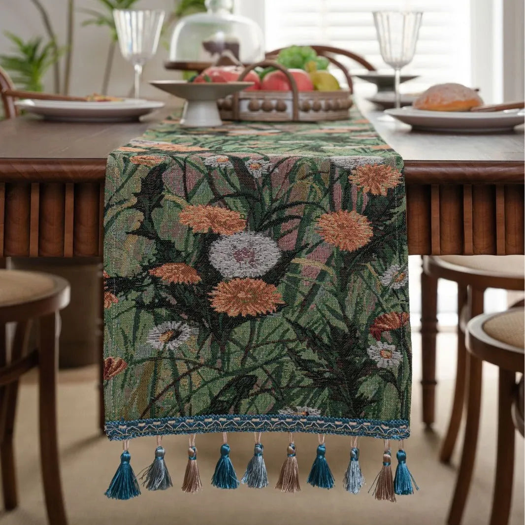 Beige jacquard table runner with floral pattern and long tassels on a wooden table.