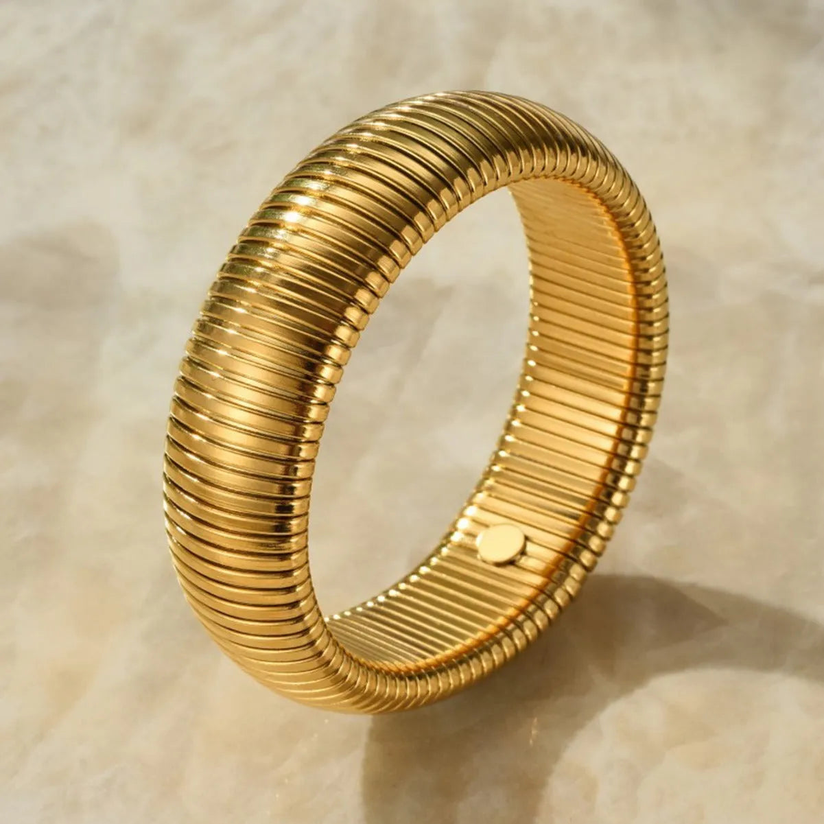 Close-up of a women's titanium steel bracelet with a vertical stripe ring pattern, shown in a gold tone finish on a wrist.