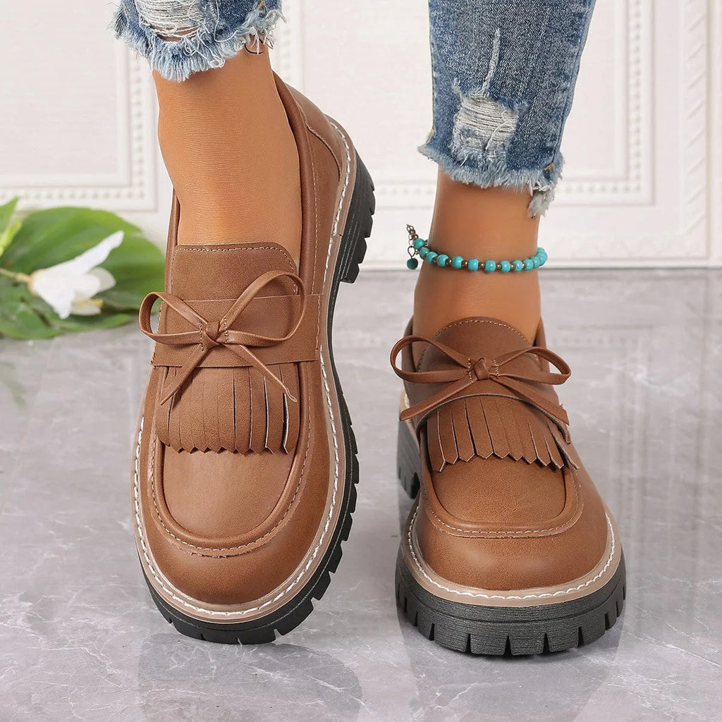 Black plus-size women's loafers with a bow and tassel detail on a chunky rubber sole.