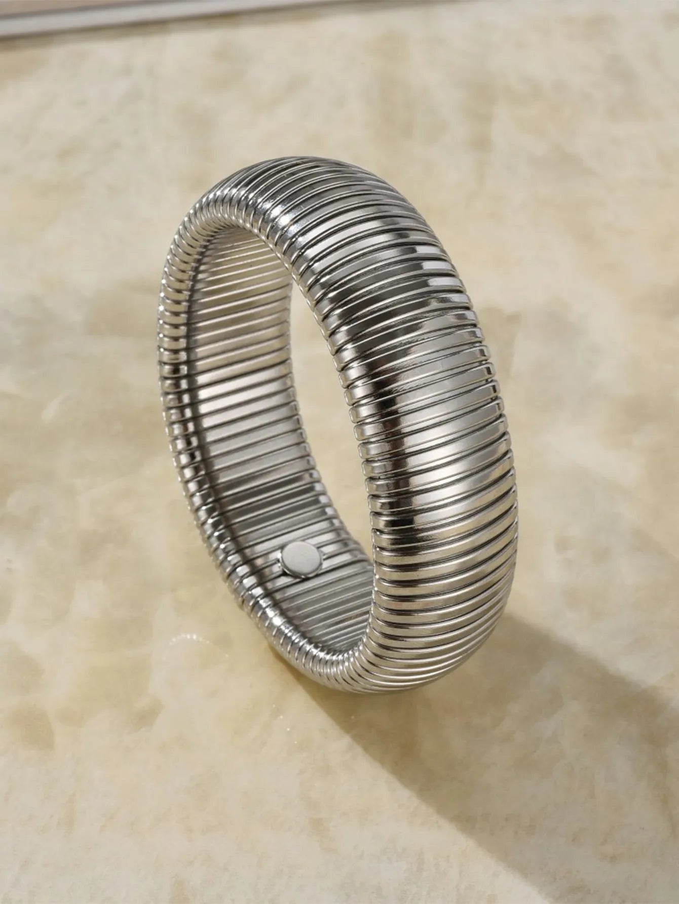 Close-up of a women's titanium steel bracelet with a vertical stripe ring pattern, shown in a gold tone finish on a wrist.