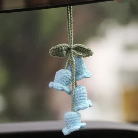 Green and white knitted wool car plant decoration with hanging rope on a car dashboard