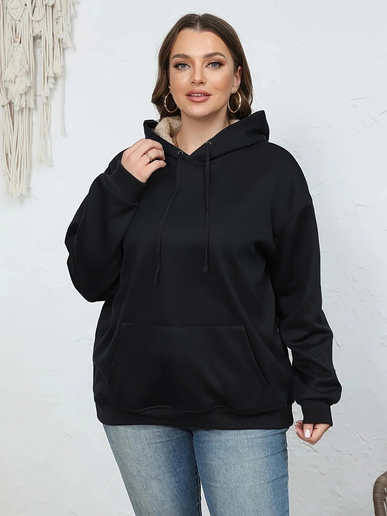 A woman wearing a loose thick black hooded sweater with side pockets and a 3D textured pattern.