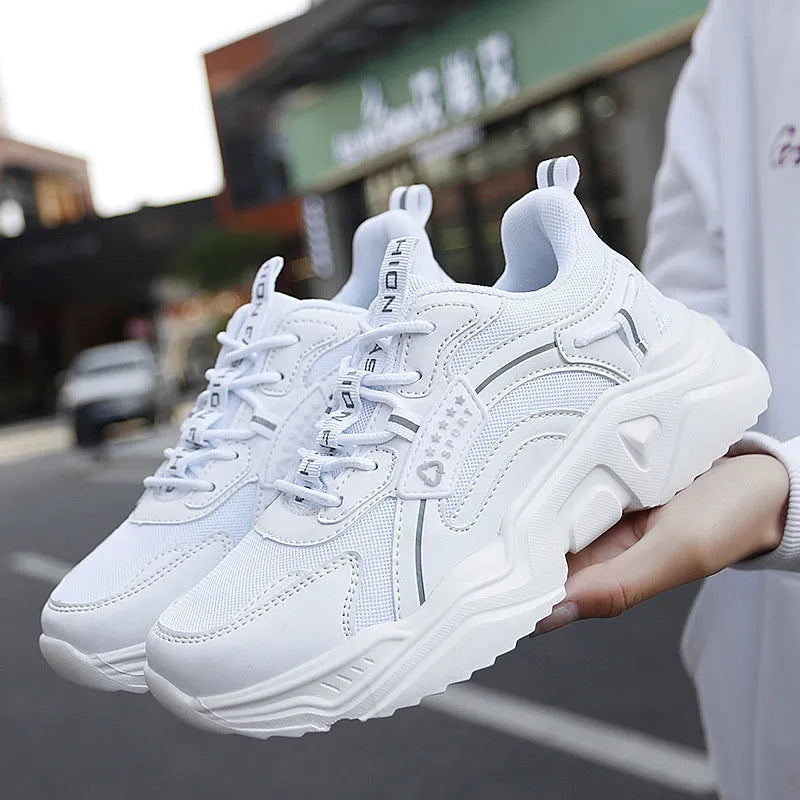 Women's white thick-soled casual sneakers with mesh upper and buckle detail on a light background.