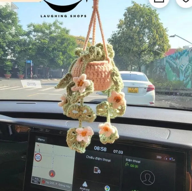 Green and white knitted wool car plant decoration with hanging rope on a car dashboard