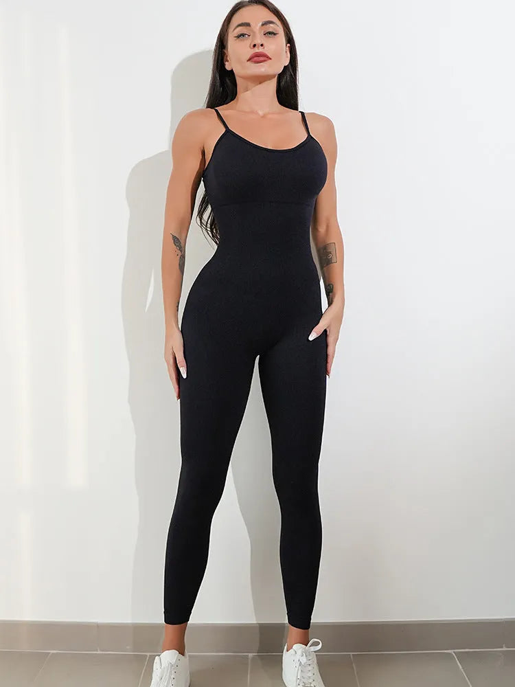 Woman wearing a black sleeveless unitard jumpsuit with spaghetti straps, showcasing the form-fitting tummy control design.