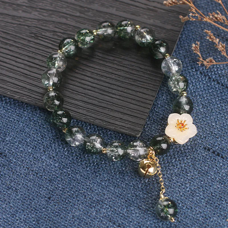 Green Phantom quartz crystal bracelet with white jade flower on a plain background