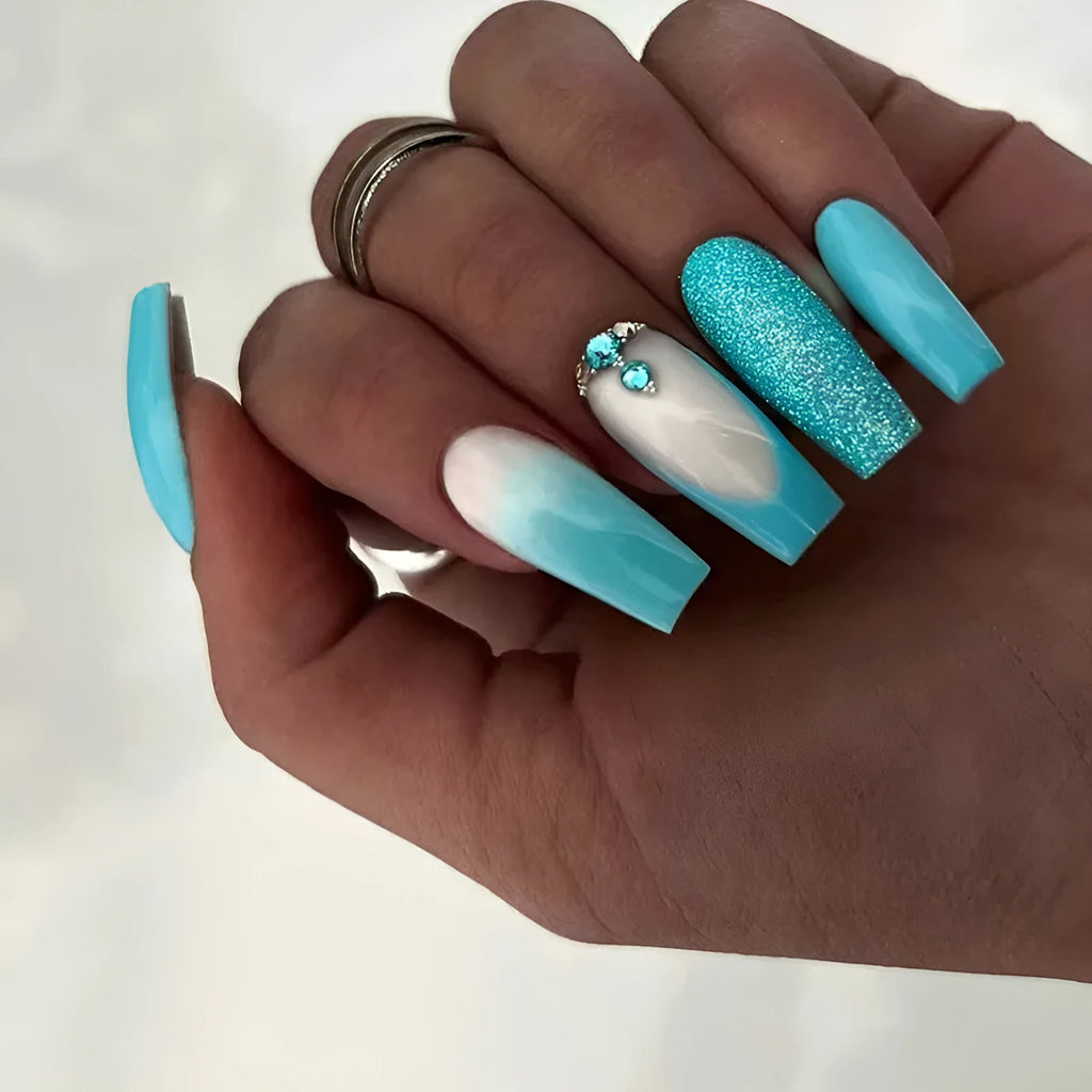 Long solid colour ballet artificial nails with blue diamond glitter glue on a pink background